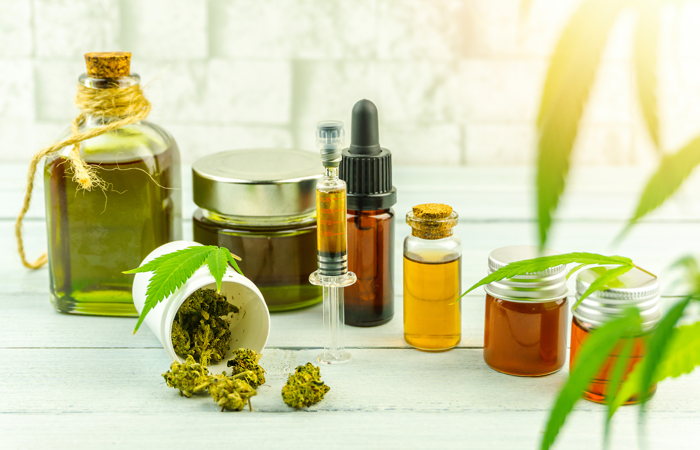 CBD Cannabidiol Oil Glass Bottles, Pills Flower Buds and Cannabis Leafs on Bright Wooden Backdrop
